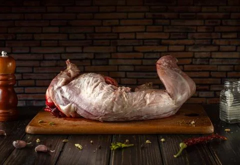 A large piece of rabbit meat rests on a wooden cutting board. Spices and ga.. Stock Photos