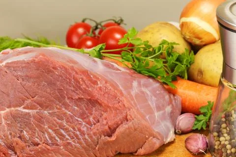 A large piece of raw pork is surrounded by several vegetables Stock Photos
