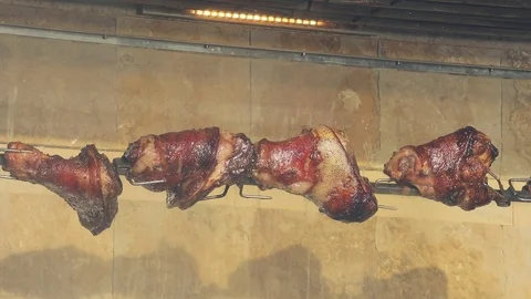 Large pieces of meat roasting on a spit. Pork legs are cooked on fire. Closeup Stock Footage 103854648