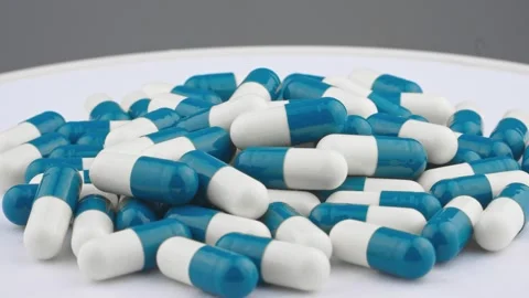 A large pile of blue and white capsules is scattered on a white surface Stock-Footage 341034411