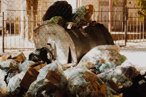 A large pile of garbage packets is lying around the full trash tank. human wa Stock Photos