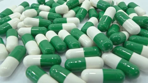 A large pile of green and white capsules is scattered on a white surface Stock Footage 341033595