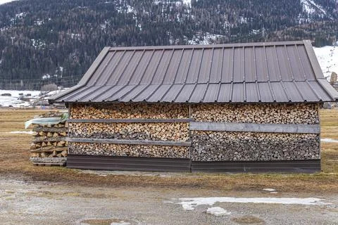 Large pile of split timber for heating stored by a rural barn in the winter 库存照片