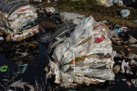 Large piles of compressed waste materials are seen near a polluted water so.. Stock Photos