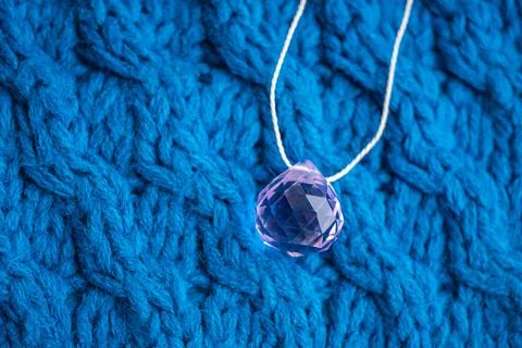 Large pink crystal with thread on a blue knitted pattern 写真素材