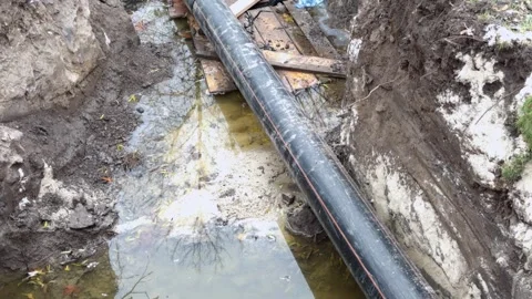 A large pipe is leaking in an excavated ditch, filling the bottom with dirt.. Stock Footage 325046733