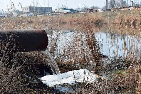 A large pipe from which sewage flows into the river. Stock Photos