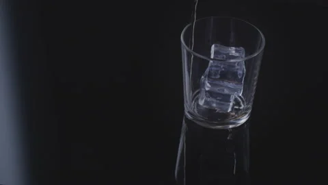 Large plan in a glass with two ice cubes pour whiskey on a black background Video stock 131065203