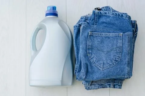 Large plastic bottle of liquid powder and a stack of denim items on the table Stock Photos