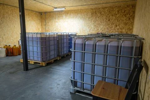Large plastic containers filled with dark liquid sit on wooden pallets Stock Photos