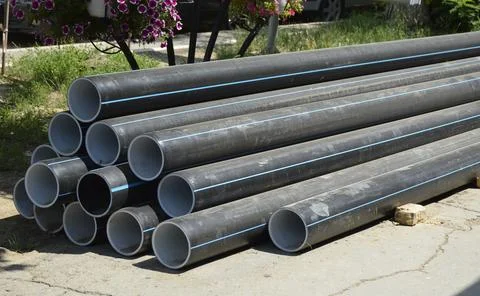 Large plastic pipes lie in a large pile on the street Stock Photos