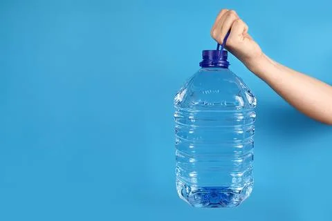 Large plastic transparent bottle for bottled water in man hand on blue wall Stock Photos