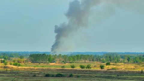 A large plume of black smoke rises over a sparsely vegetated landscape. Stock Footage 274936019