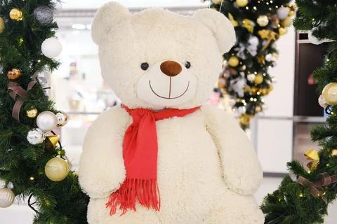 Large plush teddy bear with a red scarf is surrounded by festive decorations Stock-Fotos