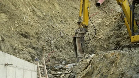 A large pneumatic hammer on an excavator breaks rocks in a quarry, on a construc Stock Footage 106579638