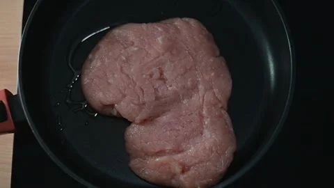 A large portion of raw meat is placed in a hot pan on a stovetop and begins to Stock Footage 339094372