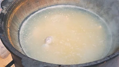 A large pot is placed over an open flame as meat cooks in boiling water. The Stock Footage 345883026