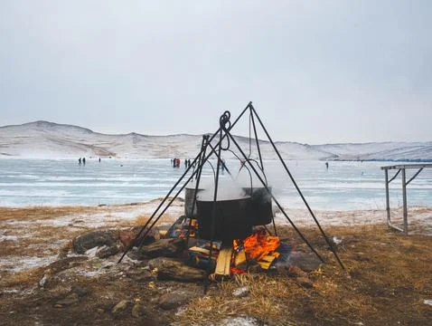 A large pot is simmering over a fire situated near a frozen lake Stock Photos