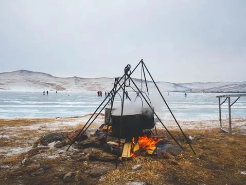 A large pot is simmering over an open fire close to a body of water Stock Photos