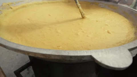 Large pot of yellow cornmeal mixture being stirred with a wooden spoon over a Stock Footage 339286431