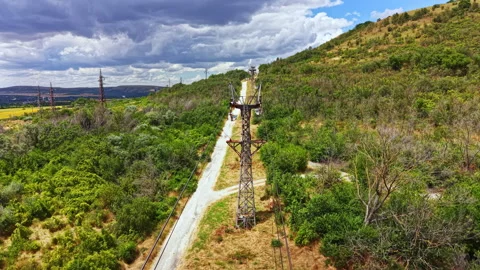 Large power lines run along a dirt road in a green area with hills and clouds in Stock Footage 340884427