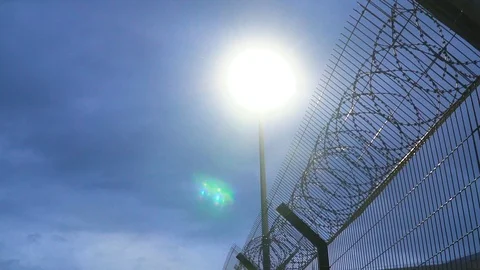 Large prison fence with barbed wire at night lit by a lantern Stock Footage 111321308
