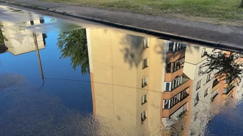 Large puddle on asphalt road reflecting a yellow apartment building Видео 340261195