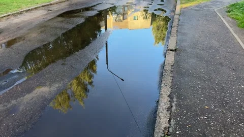 Large puddle on asphalt road reflecting a yellow apartment building Видео 340261371