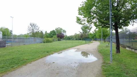 Large puddle on dirt path next to a green golf driving range Stock Footage 332707750
