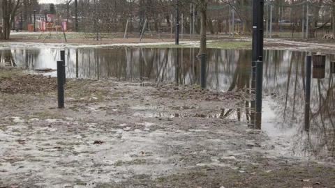 Large puddle reflecting playground in urban park during messy spring thaw Video stock 329640705