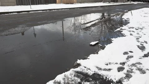 A large puddle on the road against the background of snow in winter during a Stock Footage 315513075
