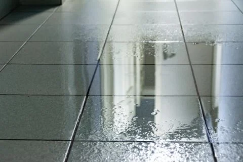 A large puddle on the tiled floor was caused by water from the ceiling as a r Stock Photos
