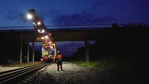 Large rail construction machine illuminated at night with workers on-site Stock Footage 313470094