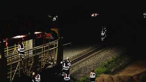 Large rail construction machine illuminated at night with workers on-site Stock Footage 313470129