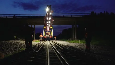 Large rail construction machine illuminated at night with workers on-site Stock Footage 313470132