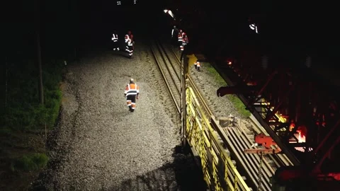 Large rail construction machine illuminated at night with workers on-site Stock Footage 313470147