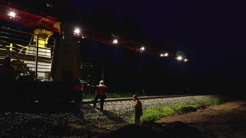 Large rail construction machine illuminated at night with workers on-site Stock Footage 313470157
