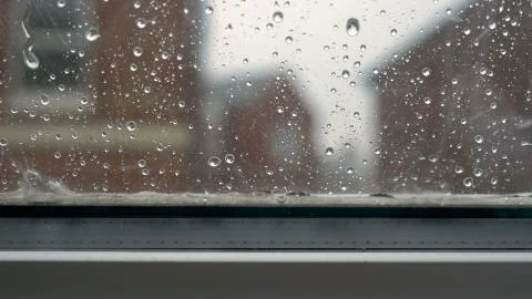 Large rain drops strike open window pane during heavy shower in England 库存照片