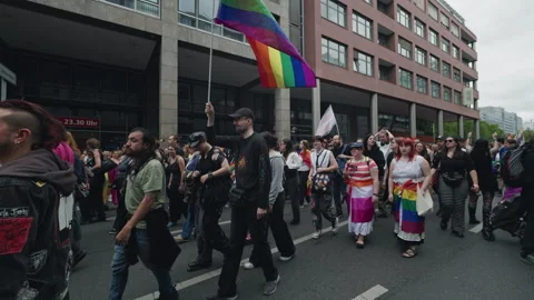 A large rainbow flag on a tall pole rises above a diverse crowd of marchers in Stock Footage 346239387