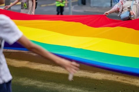 Large Rainbow Pride Flag Carried by Participants at Outdoor Event. Stock Photos