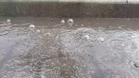 Large raindrops are pounding on the puddle, creating large bubbles and splashes Stock Footage 239633140