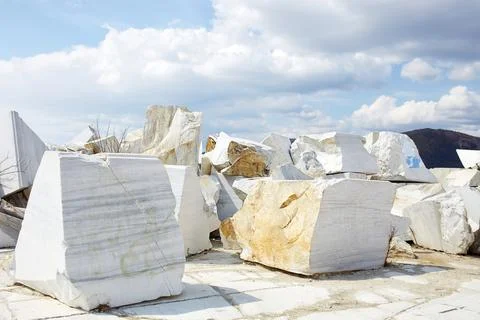 Large, raw marble blocks are scattered throughout a quarry site. Stock Photos