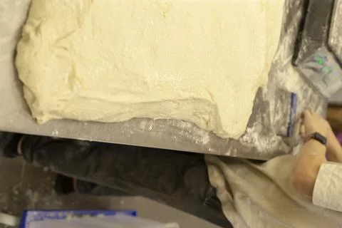 Large rectangle of raw bread dough on floured workbench with baker hands nearby Stockfoto's