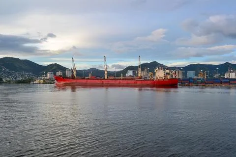 Large Red Cargo Ship Docked at Bustling Port with Cityscape Stock Photos
