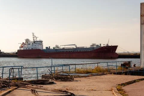 Large red cargo ship rests at harbor dockside. Sunlight casts warm glow over Stock Photos