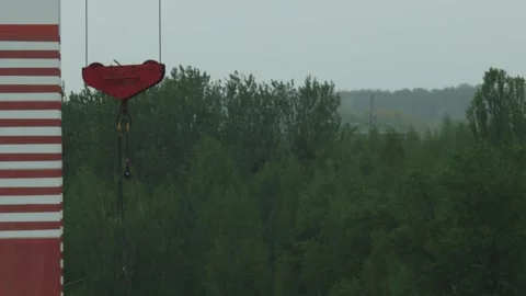 Large red crane hook suspended from towering construction crane mast with red Stock Footage 335763185