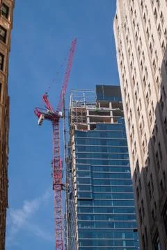 Large red crane running up the side of a skyscraper with buildings on the sid Stock Photos