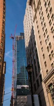 Large red crane running up the side of a skyscraper with buildings on the sid Stock Photos