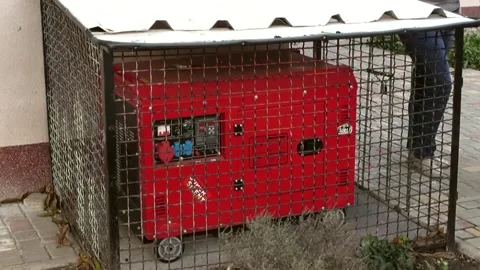 A large red diesel generator sits locked behind bars. Stock Footage 324766492