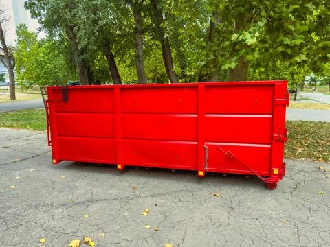 A large red dumpster sits on a concrete path. The ground is covered with fall Stock Photos